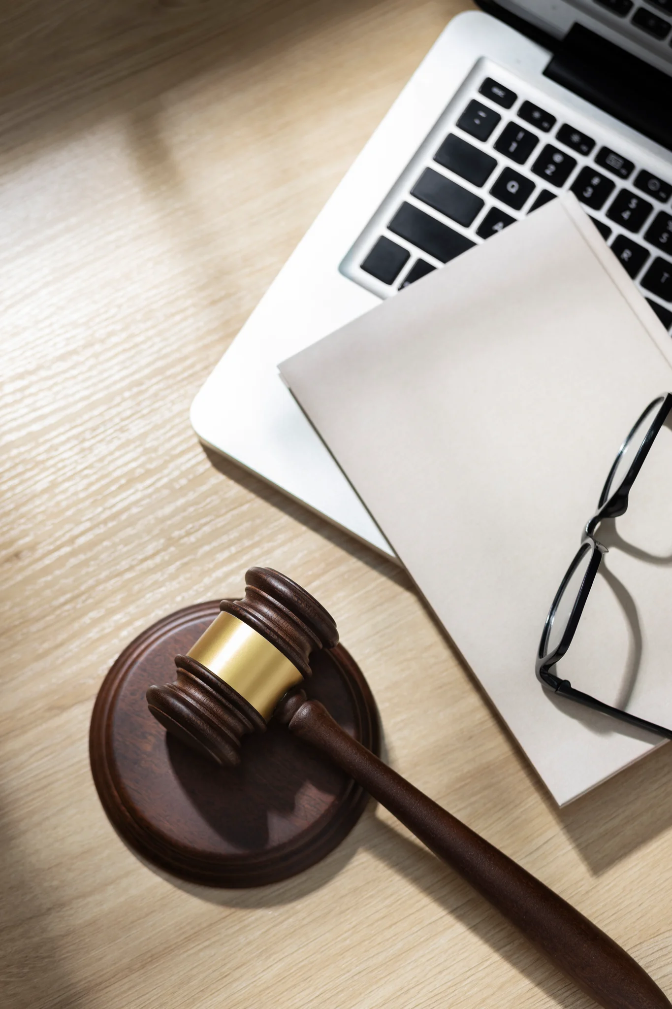Maillet, lunettes et dossier posés sur un ordinateur portable, sur un bureau en bois clair