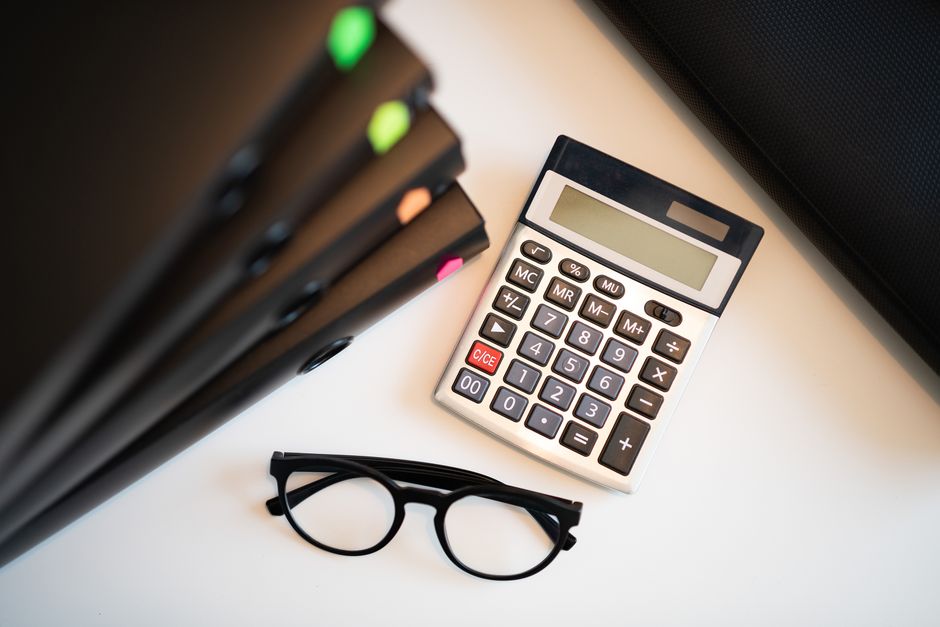 Calculatrice, lunettes et dossiers de chiffrage d'un préjudice sur un bureau