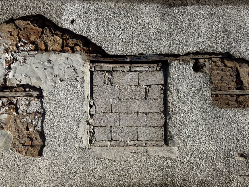 Façade de maison fissurée, enduit décollé laissant apparaître la maçonnerie