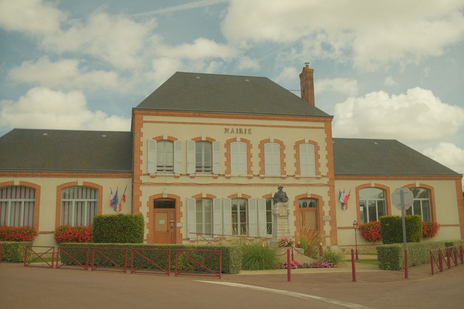 Façade d'une mairie française avec drapeaux et massifs fleuris