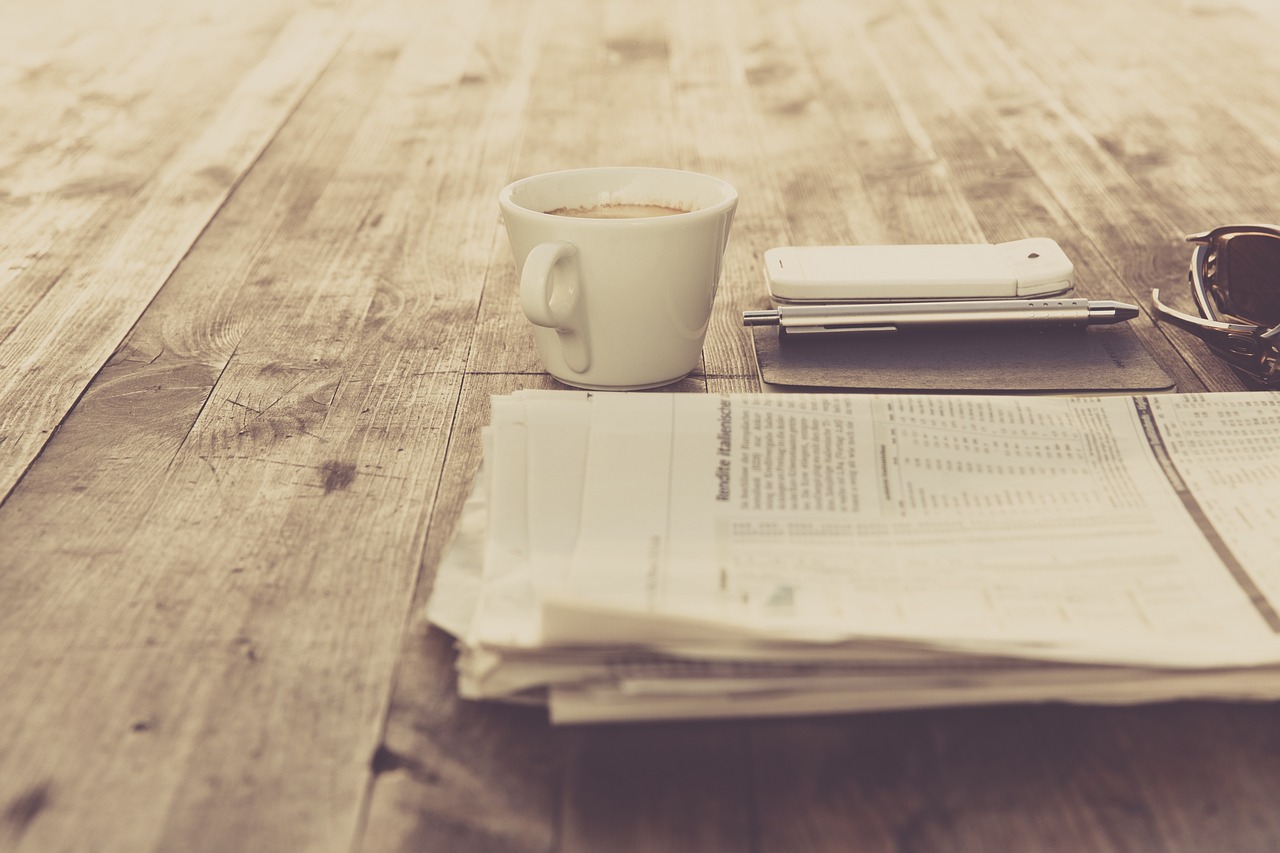 Journal, tasse de café et stylo posés sur une table en bois